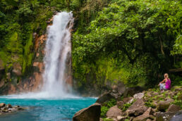 Female hiker resting at the aqua marine waterfall at the Catarata Rio Celeste in Parque Nacional Volcán Tenorio.