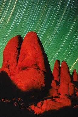 Star trails agains glowing red rocks at Joshua Tree National Park, California.