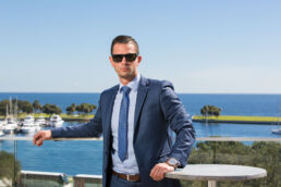 Modern business professional headshot in St. Petersburg, Fl of male executive in suite and tie with view of marina and Tampa Bay from the Rooftop bar.