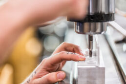 Detail of hands holding metal pieces while drilling holes in small batch commercial products in central Florida manufacturing facility.