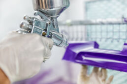 Industrial paint booth worker hand spraying products purple at Tampa Bay manufacturing facility.