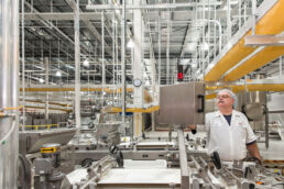 Employee in white adjusts production equipment on factory floor of food processing facility.