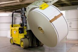 Roll clamp forklift carrying large recycled paper roll through industrial facility in Wabash, Indiana.