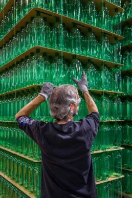 Beverage manufacturing plant employee stacks green plastic bottles at Ball Plastics Plant in New Jersey for trade magazine Hired.