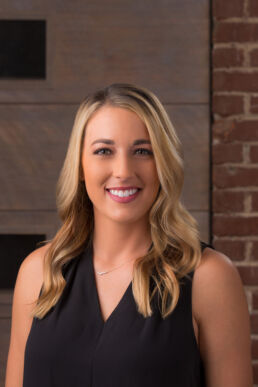 Casual employee headshot of young woman with red brick wall on location at architecture office on downtown St. Petersburg, Fl.