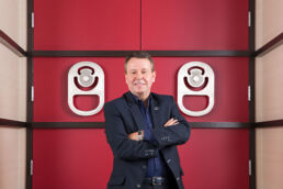 Cott Corporation CEO portrait in Tampa, Fl standing with arms crossed in front of vibrant red doors at corporate office in Tampa, Florida.