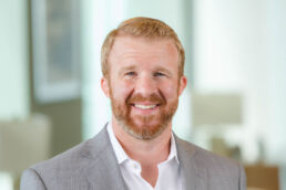 Casual business profile photo of young male with red beard in gray blazer at his downtown Tampa office.